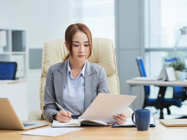 medium-shot-young-asian-woman-suit-sitting-desk-office-reading-document
